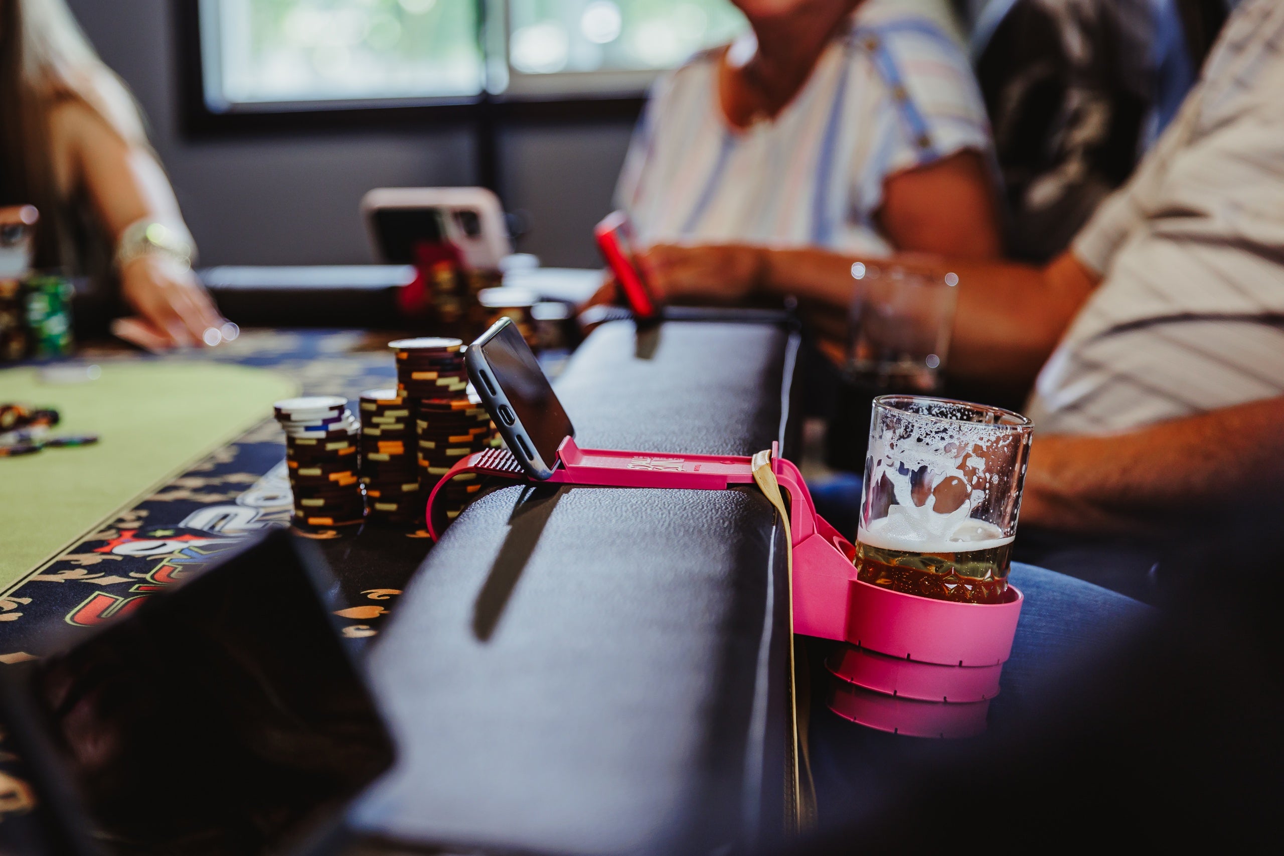 An All In Cup Holder mounted on a poker table, safely securing a beer while streaming on phone