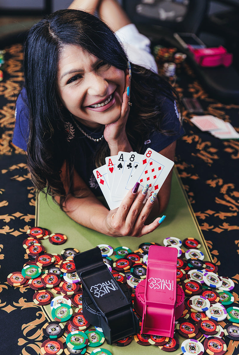 Woman laying on ground in front of poker chips and All In Cup Holders while holding up a full house cards